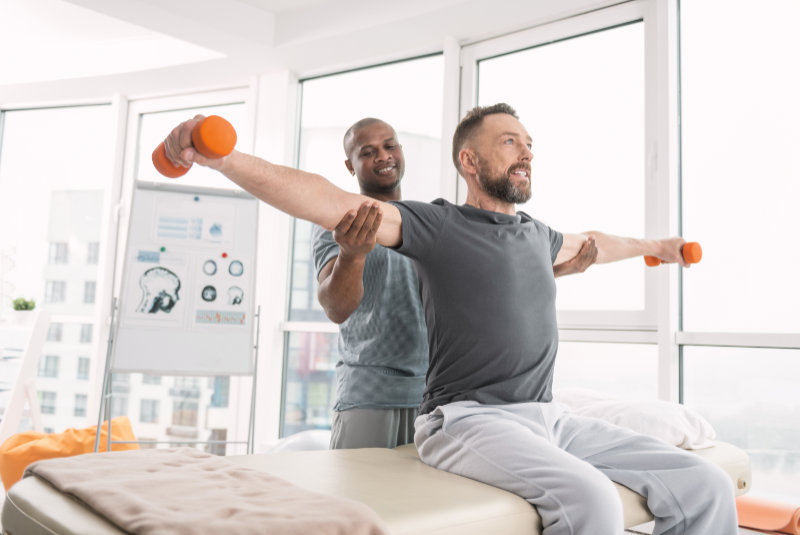 Nice positive doctor standing behind his patient while fixing his hands in the right position