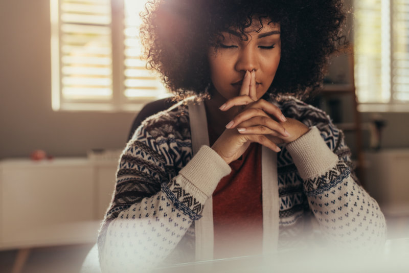 African female sitting at her work desk and thinking with her eyes closed. Stressed woman taking a break to come up with solution using mindfulness.